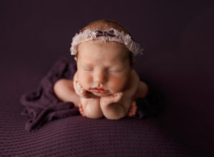 A sleeping baby in the froggy post on a deep purple blanket. Check out cottonwood OBGYN.