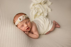 A sleeping baby laying on her side wrapped in a cream colored wrap.
