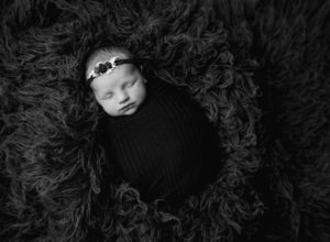 A black and white photo of a swaddled baby girl wearing a floral headband. 